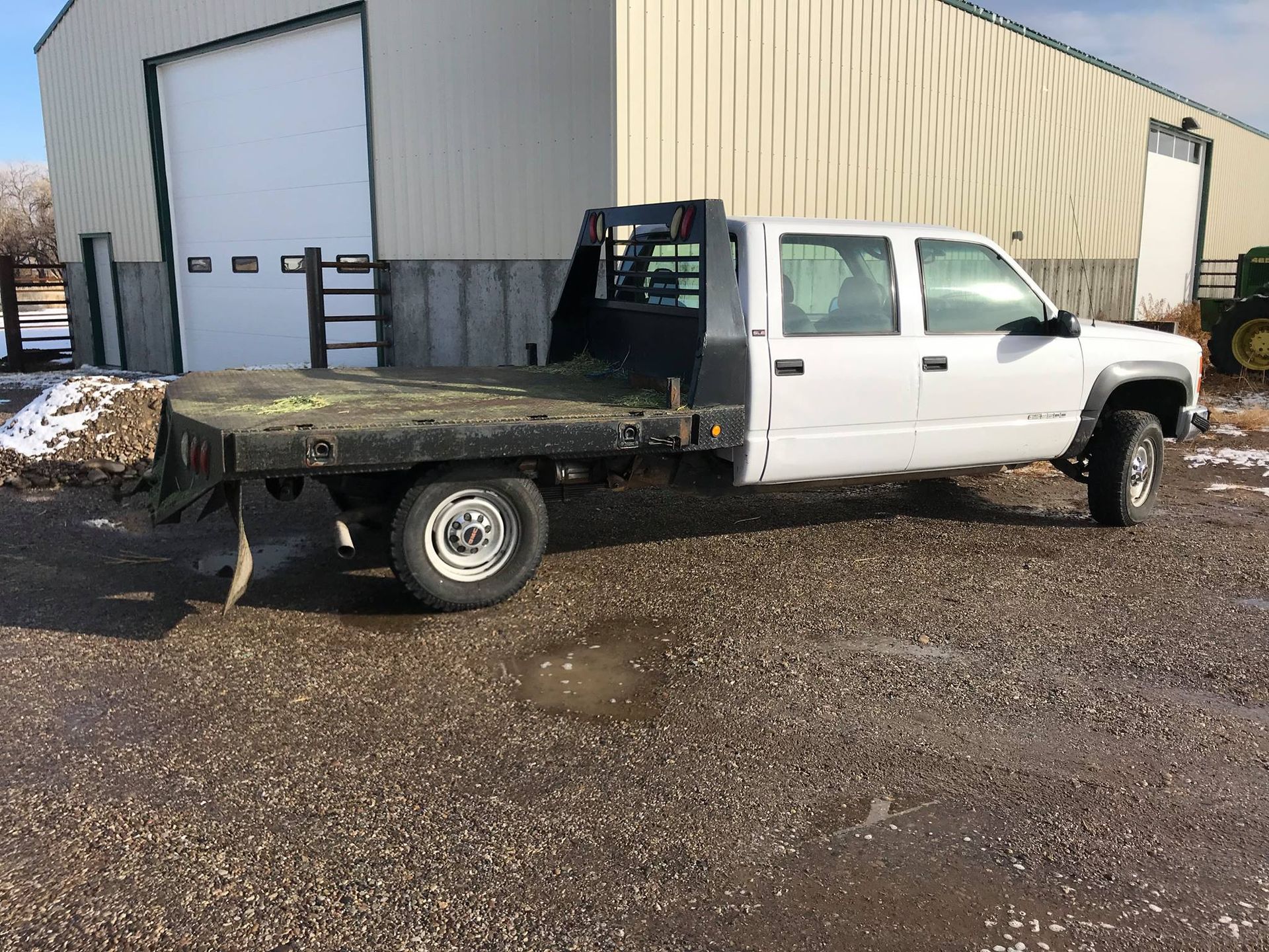 A white truck with a flat bed is parked in front of a building