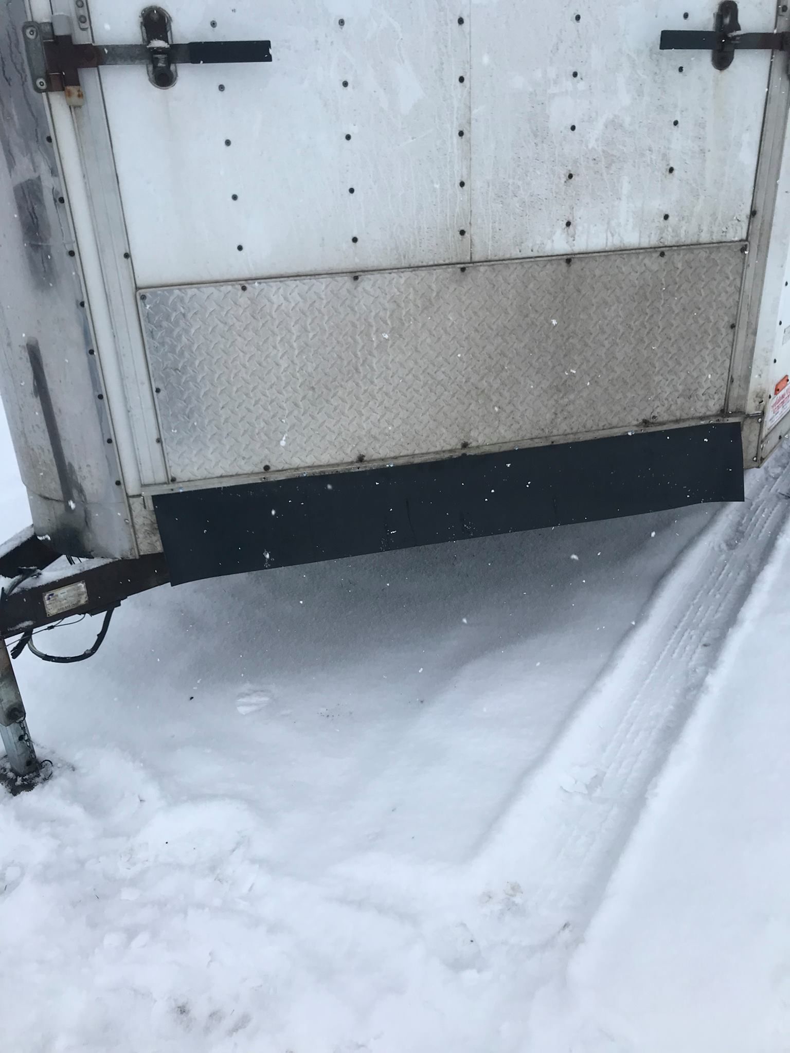 A white trailer is sitting in the snow on a snowy road.