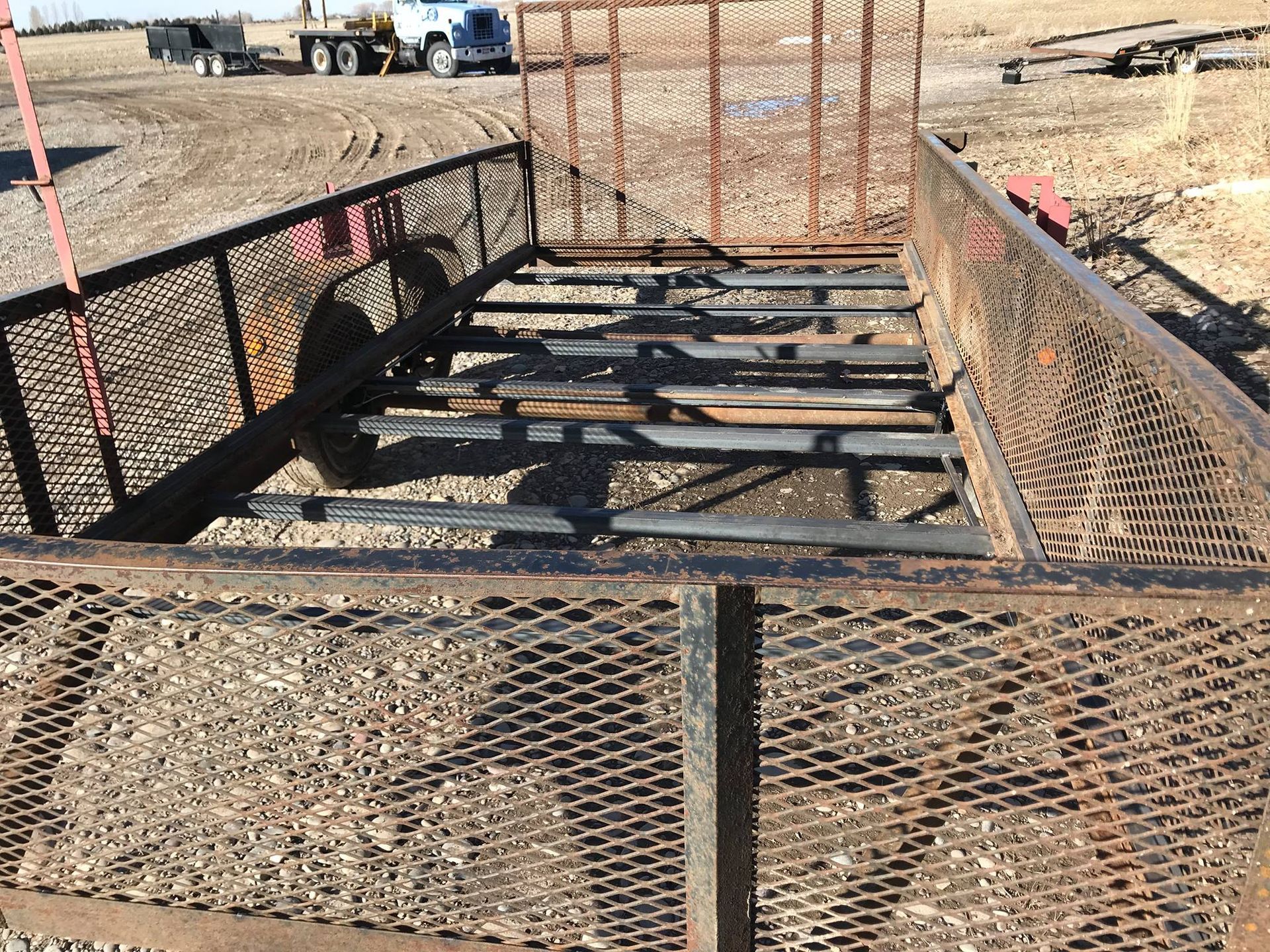 A metal trailer is sitting on top of a gravel road.