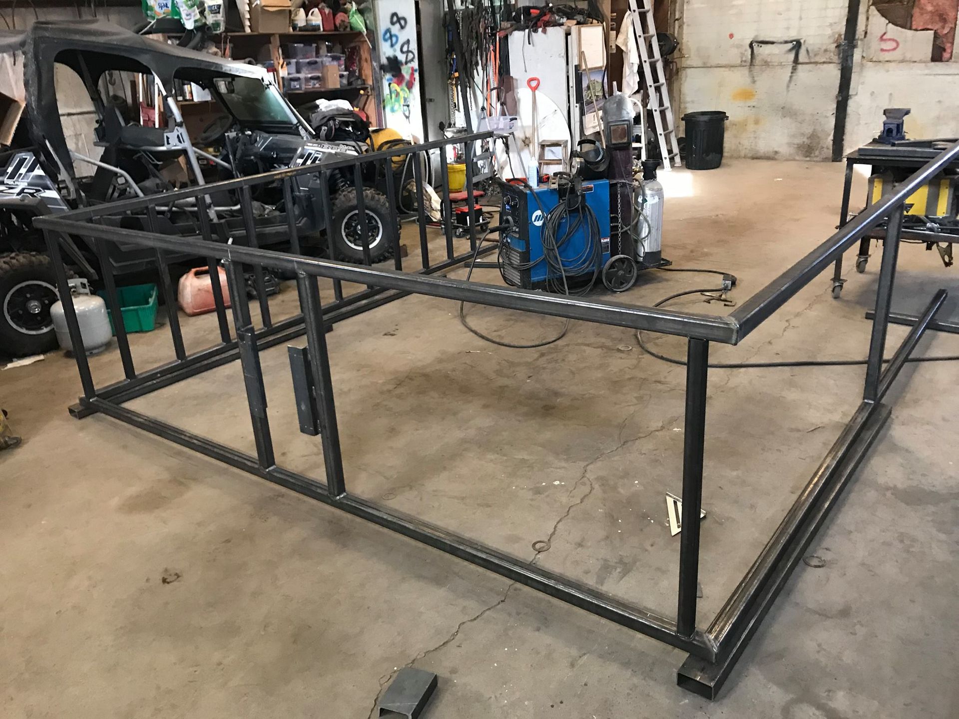 A metal frame is sitting in a garage next to a vehicle.