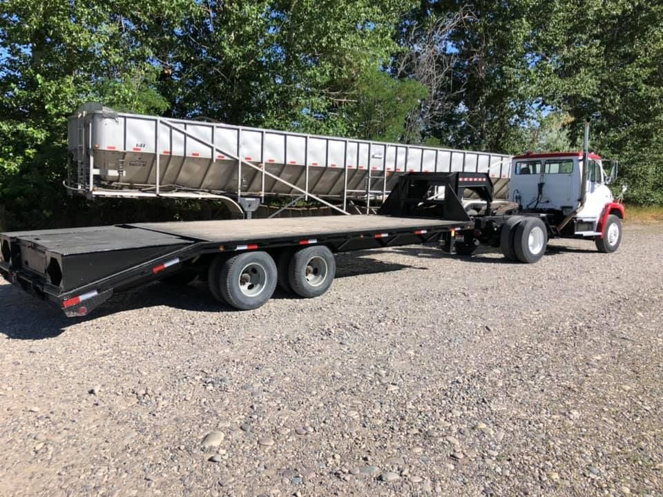 A semi truck with a flatbed trailer attached to it is parked in a gravel lot.