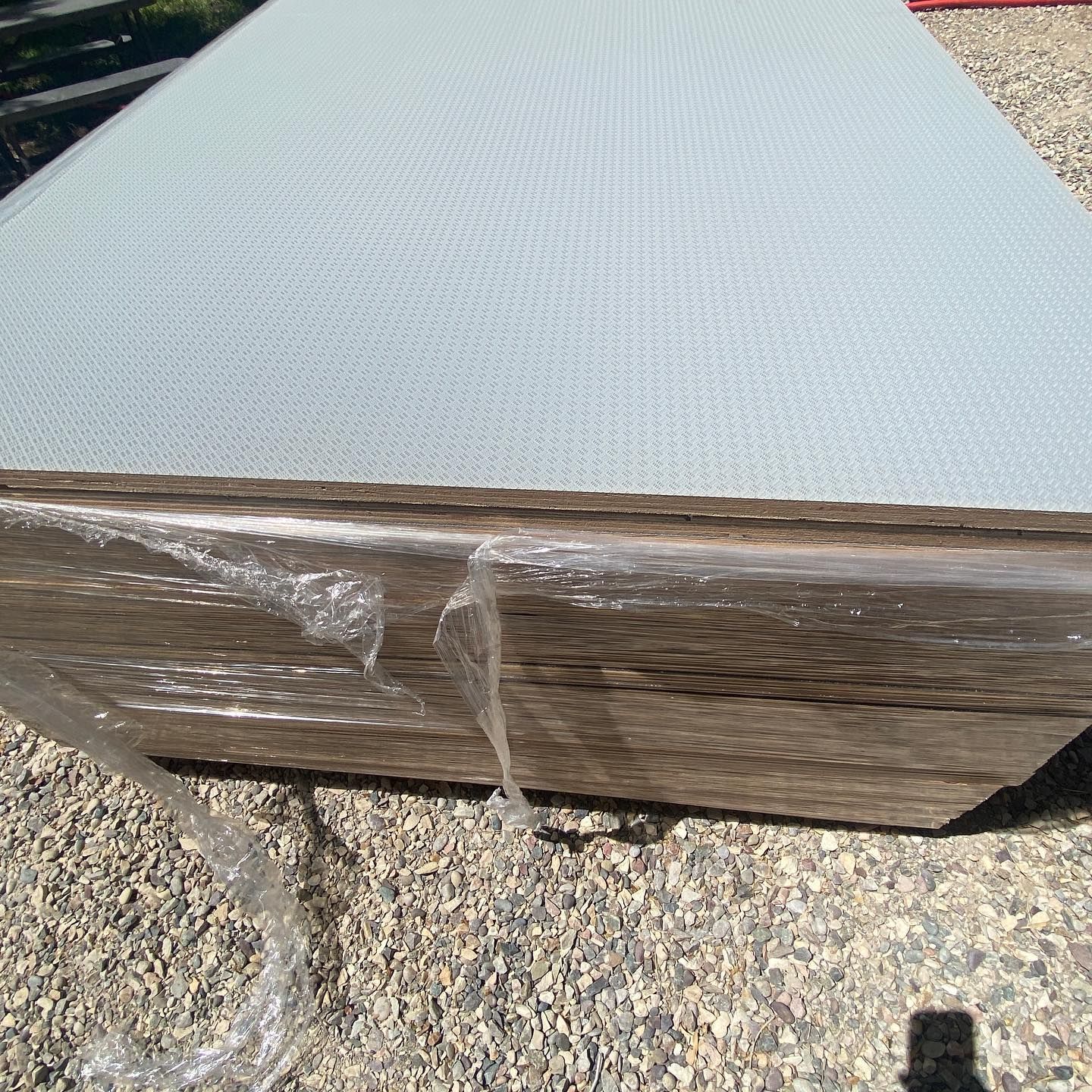 A piece of wood is wrapped in plastic and sitting on a gravel surface.