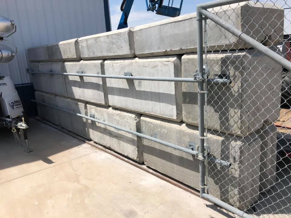 A large concrete wall is behind a chain link fence.