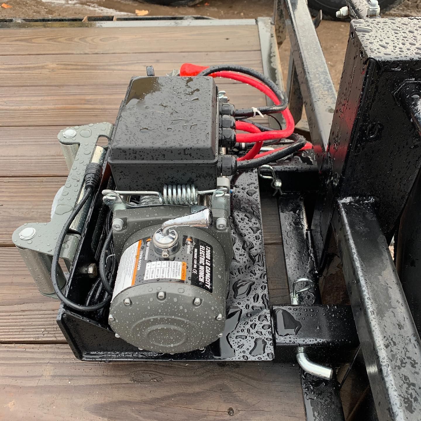 A winch is attached to a trailer on a wooden deck.