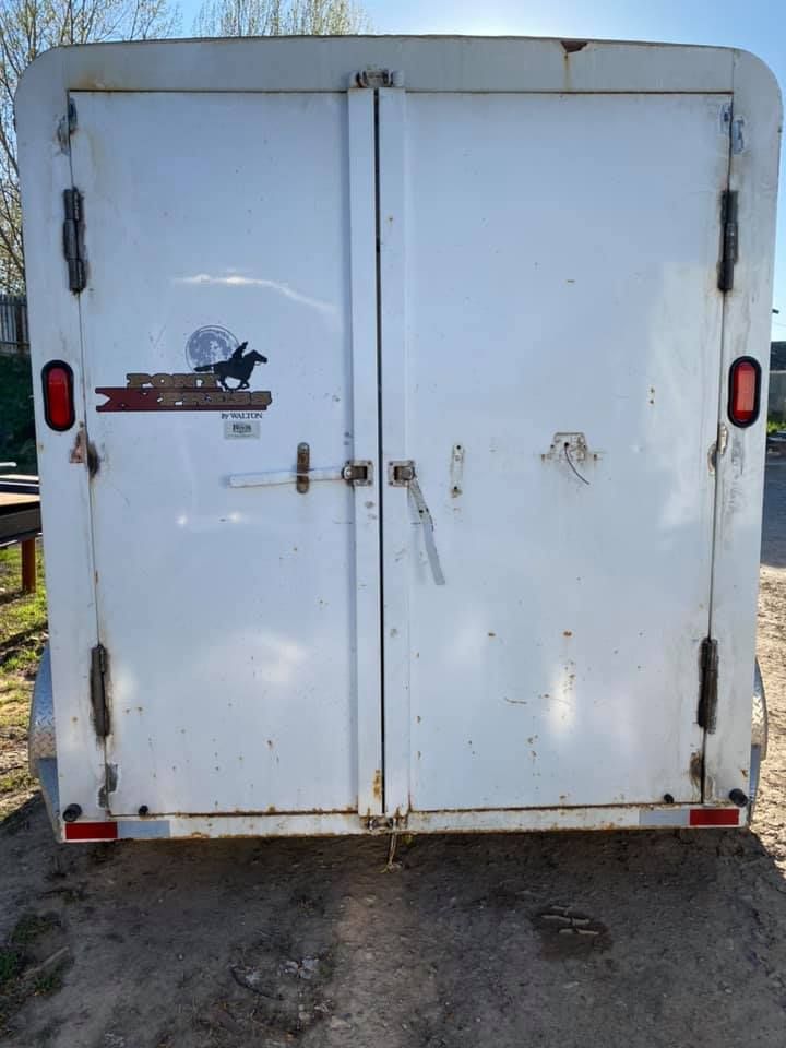 The back of a white trailer with a horse on the door.