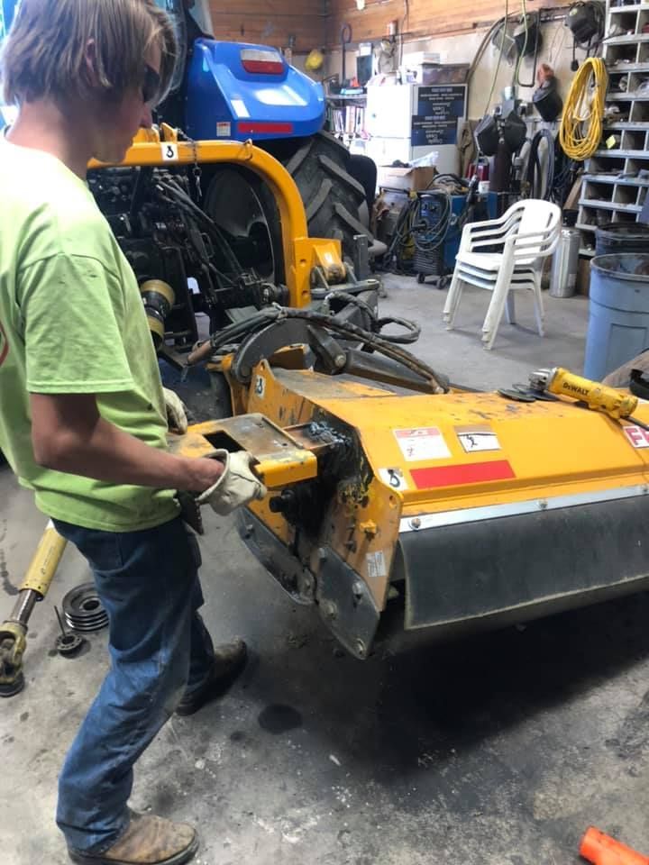 A man in a green shirt is working on a tractor in a garage.