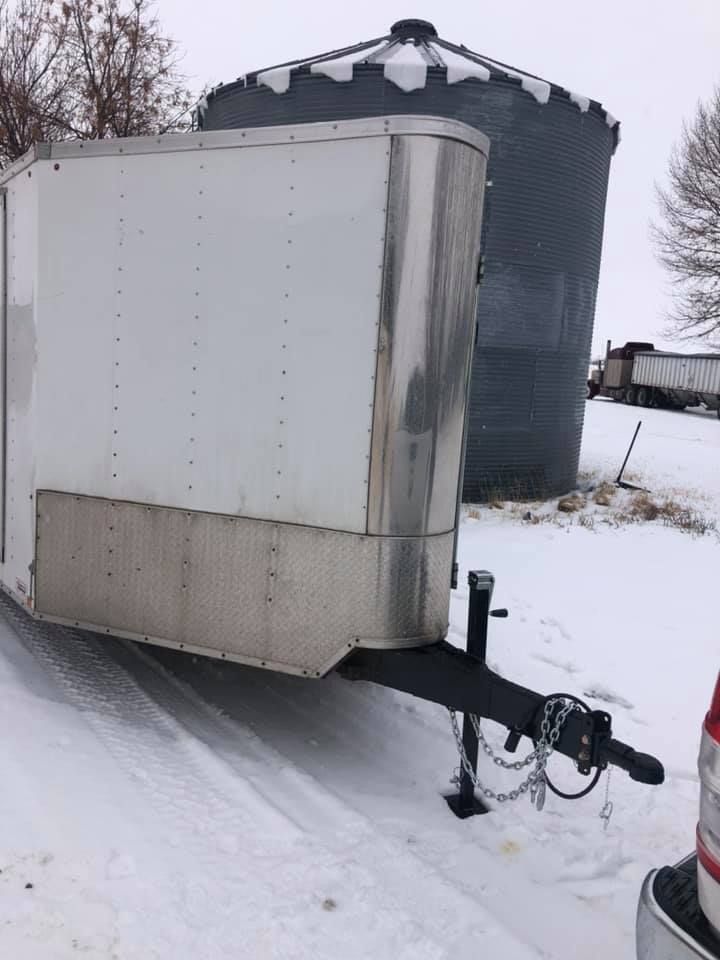 A white trailer is parked in the snow next to a truck.