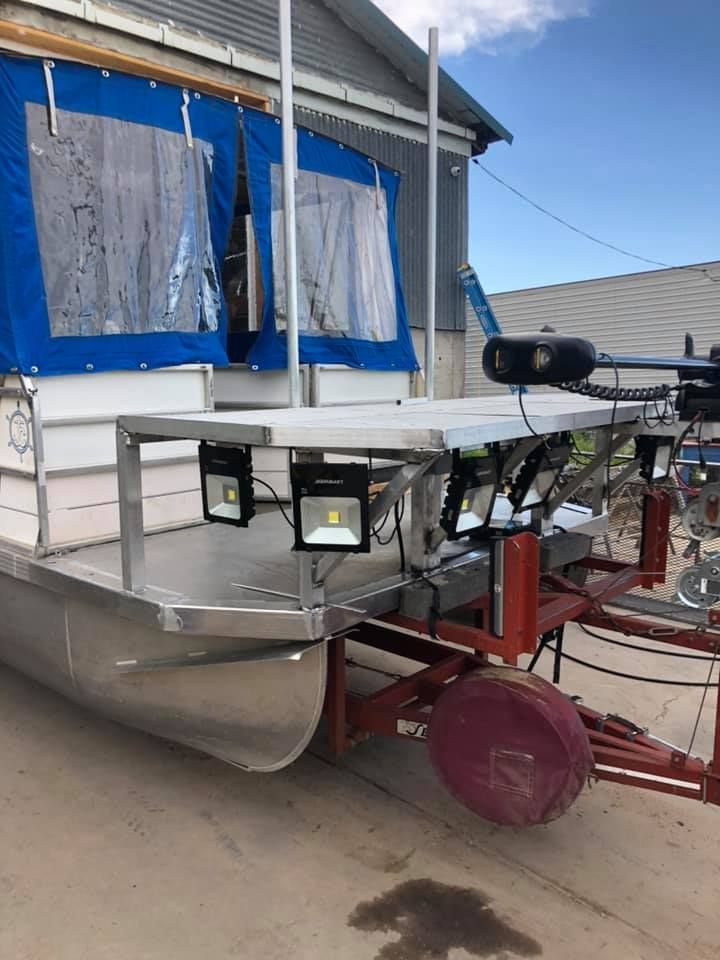 A pontoon boat on a trailer is parked in front of a building.