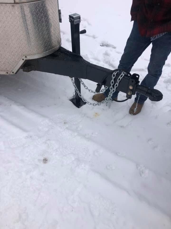 A person is standing next to a trailer in the snow.
