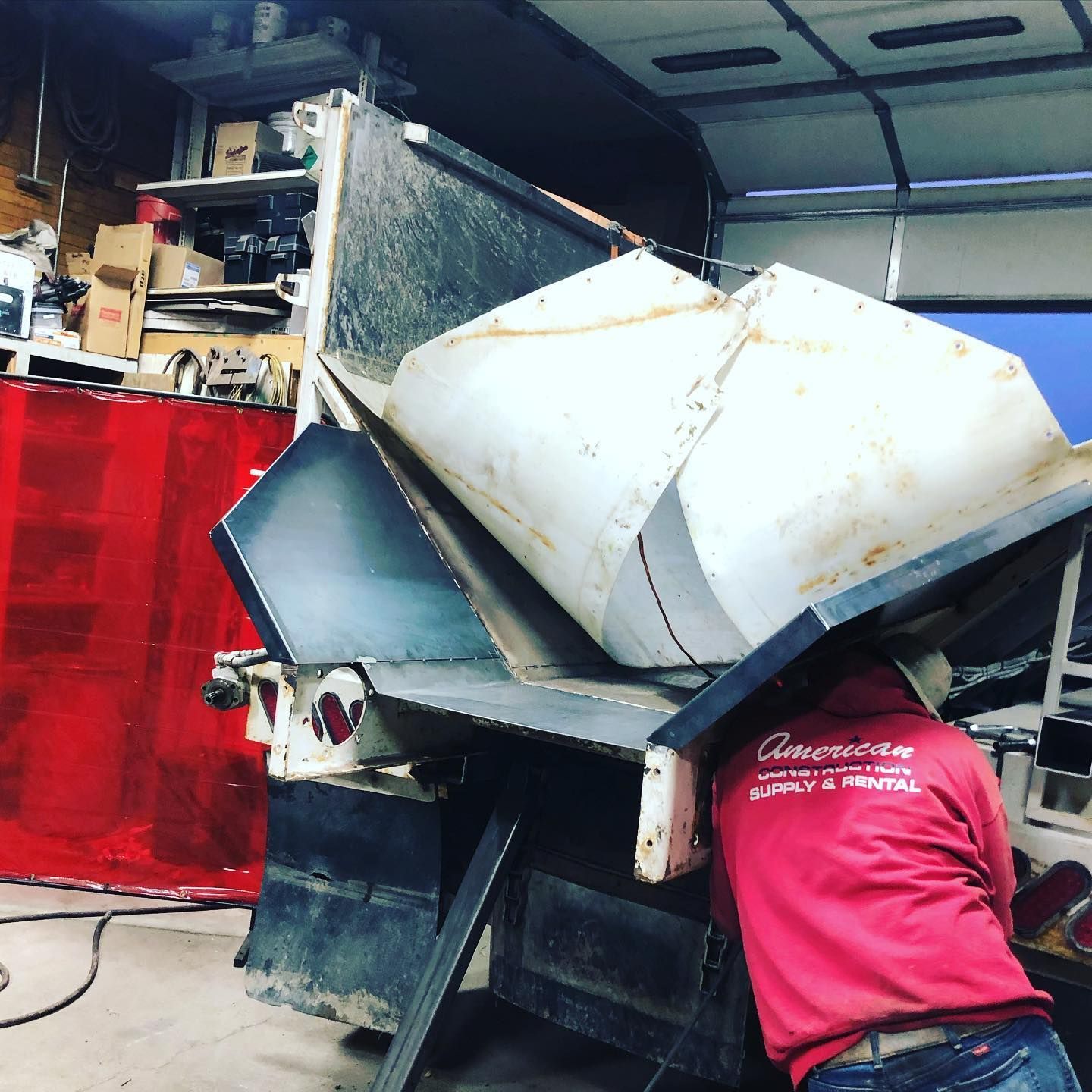 A man in a red shirt is working on a dumpster