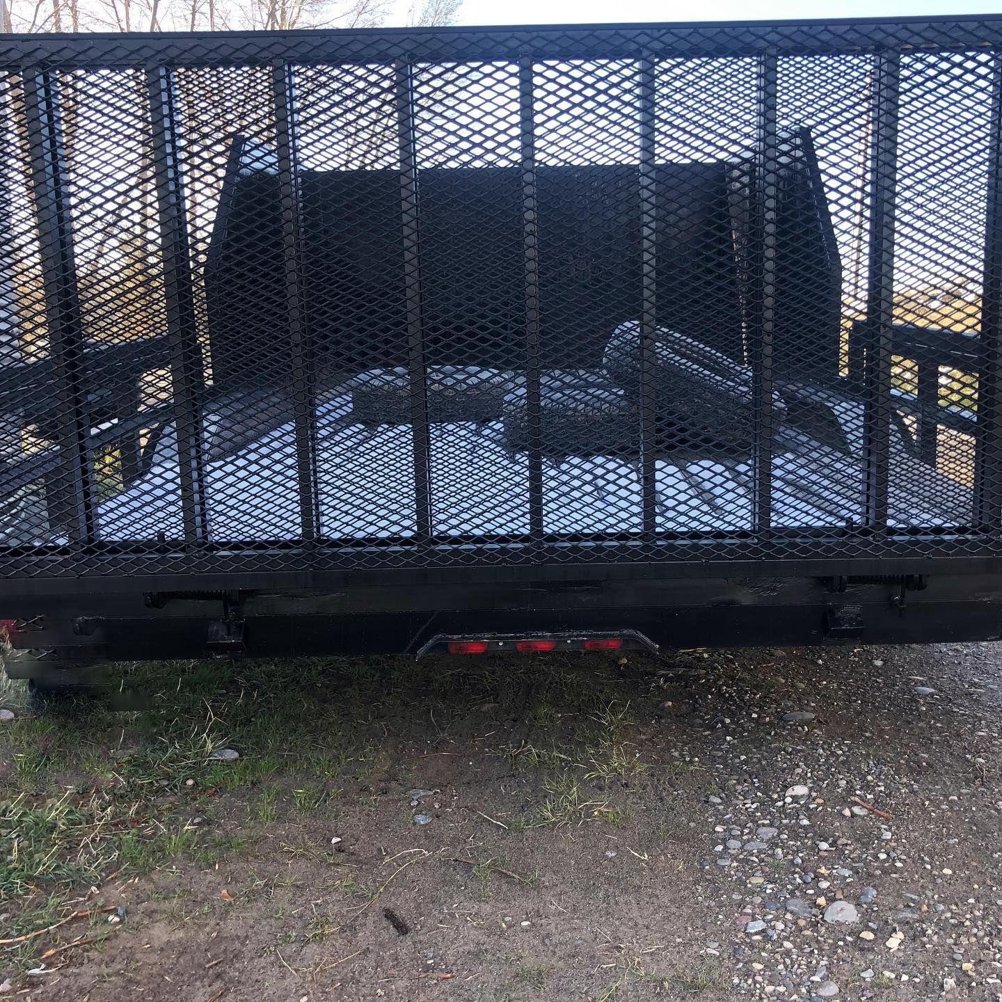 A trailer with a cage on the back of it is parked on a dirt road.