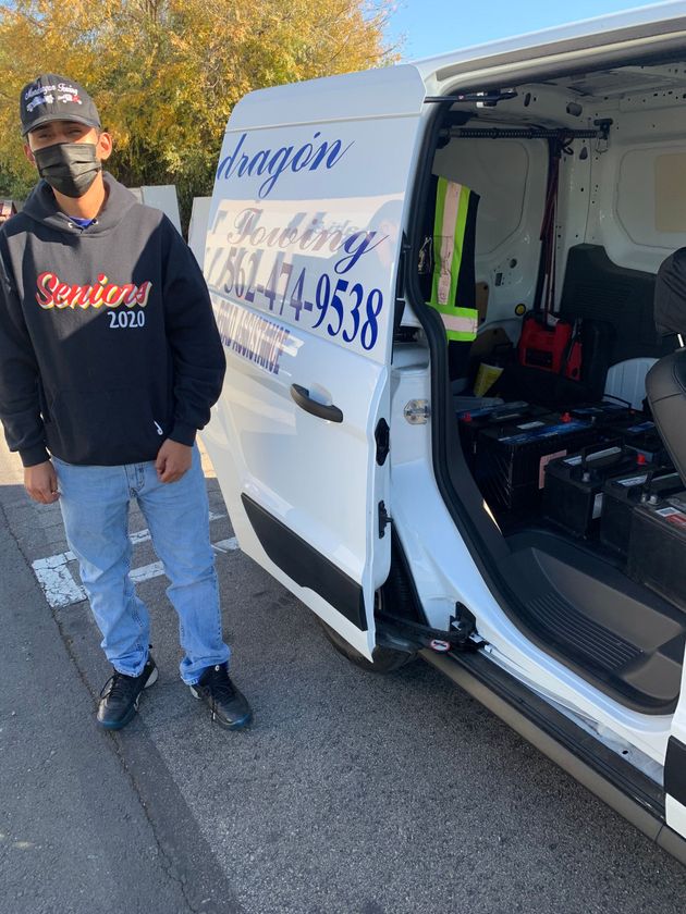 Person standing beside a white service van with its rear open, showing tools inside.