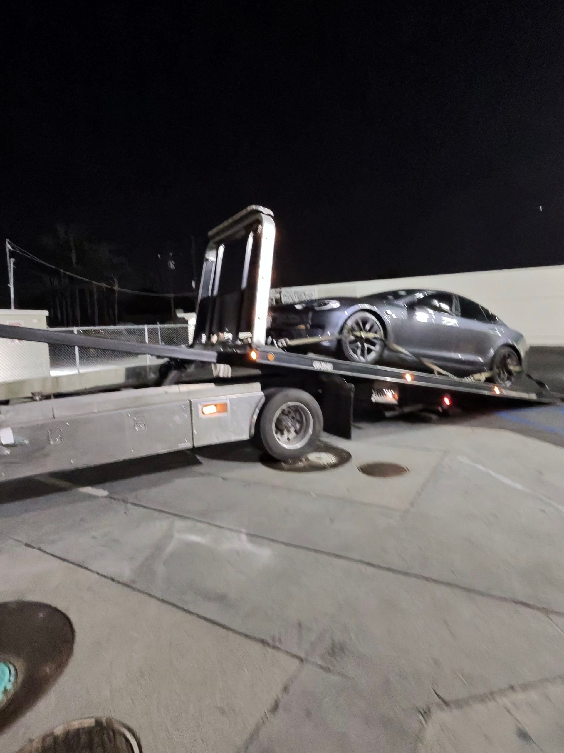 Gray car being loaded onto a tow truck at night in a parking lot.