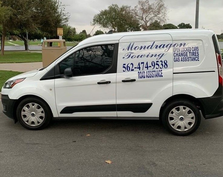 White work van with “Mondragon” signage parked on a street near a park