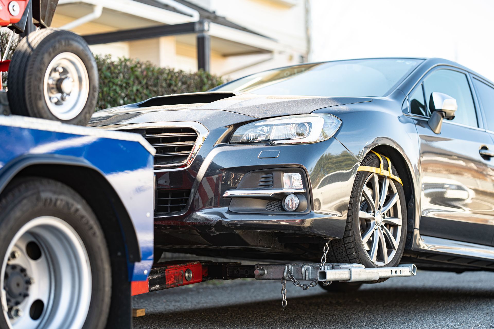 Black sedan secured on a tow truck beside a blue vehicle on a sunny street.