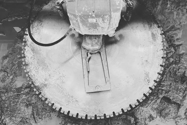 A close-up of a concrete saw cutting into a surface, showing the blade and motor.