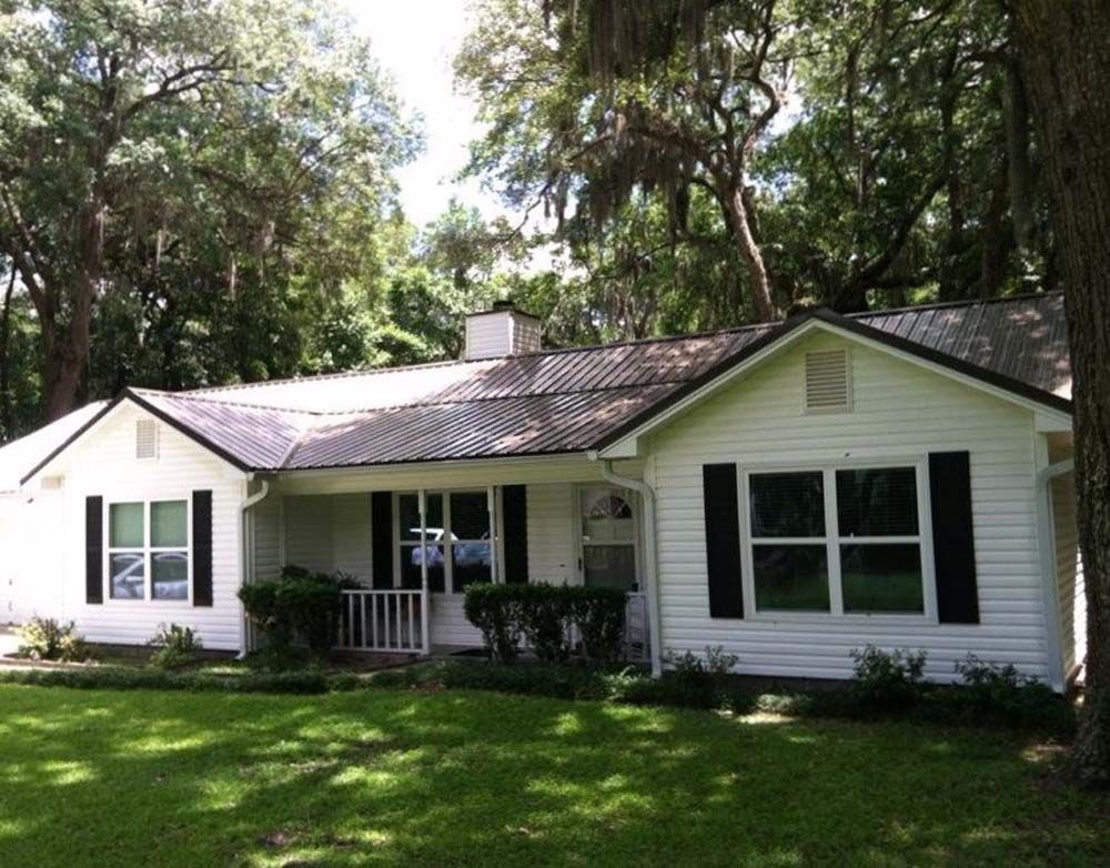 White house with black shutters, roof and trim, front yard, and trees.