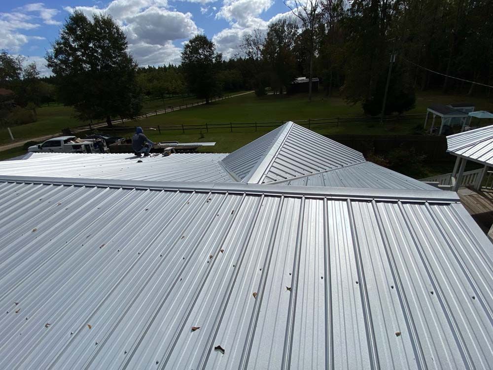 Metal roof with a ridge, a person working on it, and a landscape background.