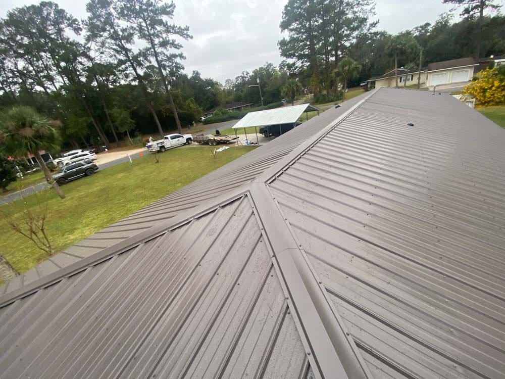 Brown metal roof of a building with a grassy yard and trees in the background.