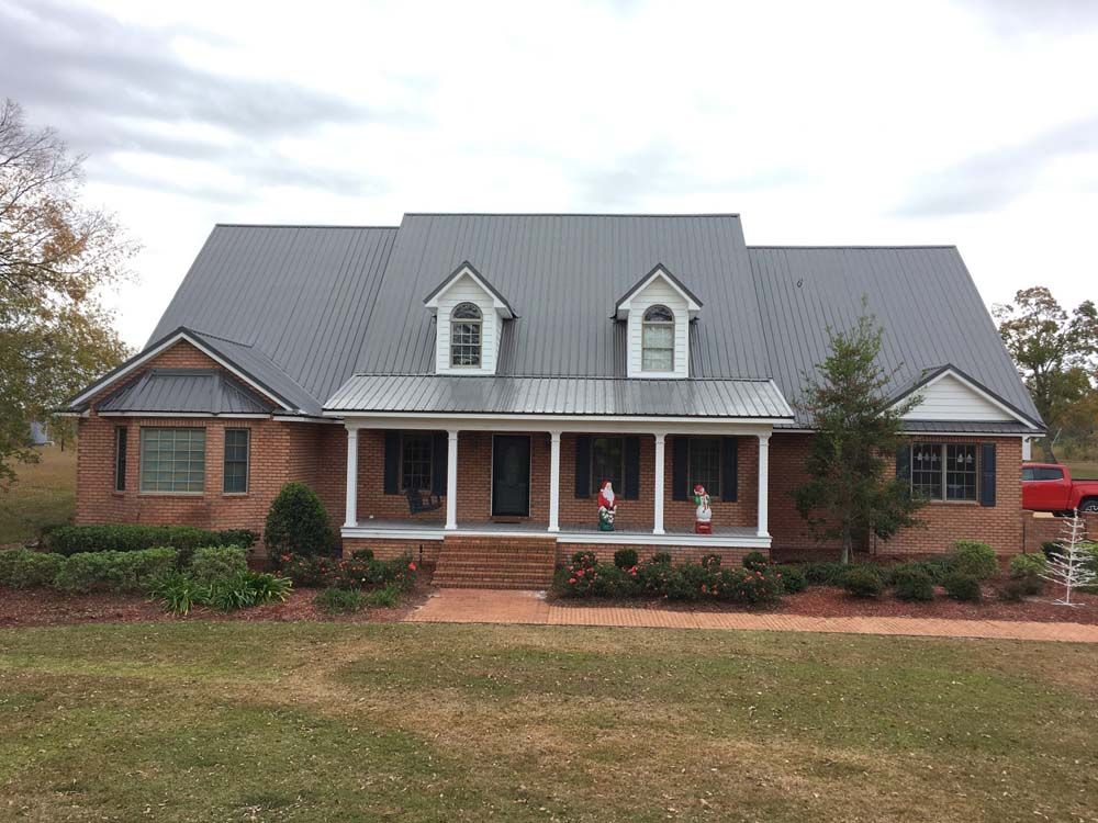 Brick house with gray metal roof, porch, and dormer windows on a cloudy day.