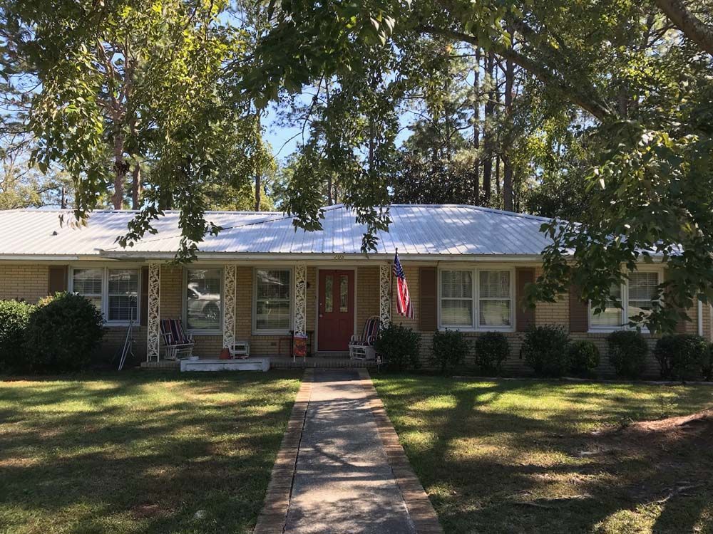 Brick ranch house with a white metal roof, red door, American flag, and a brick walkway.
