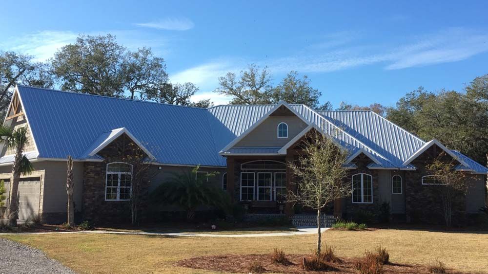 House with a light blue metal roof, beige siding, stone accents, and a blue sky backdrop.