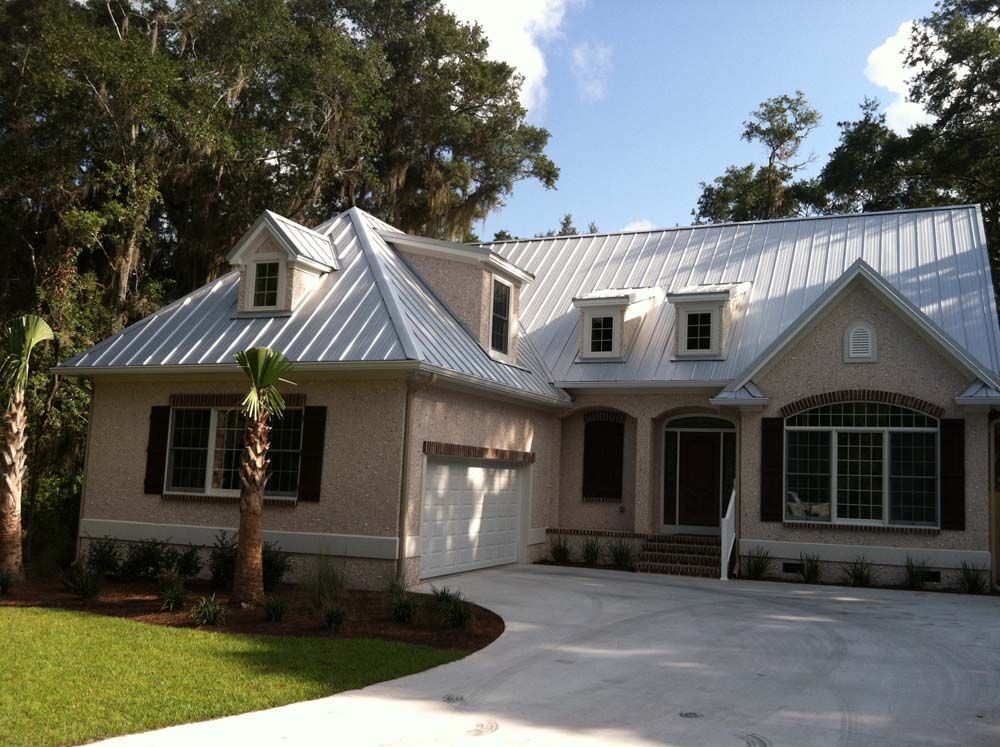 Beige house with metal roof, dormers, and a curved driveway.