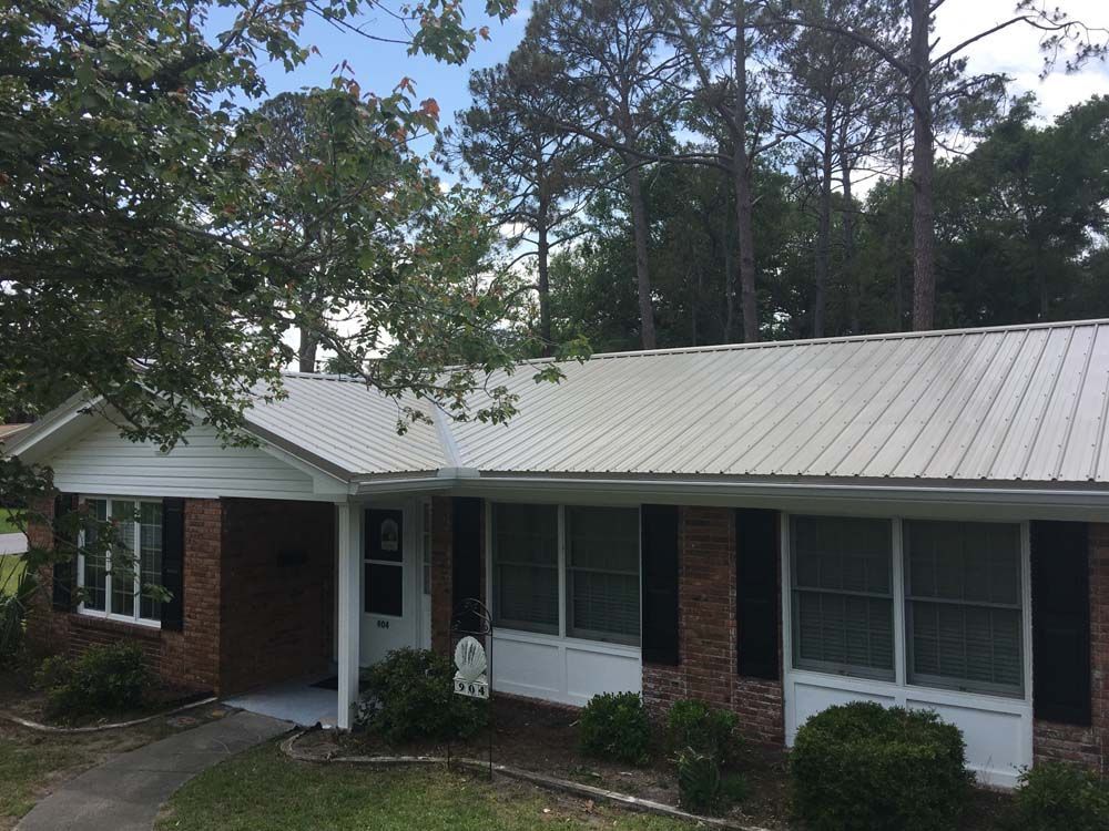 Brick ranch home with a metal roof and a porch, surrounded by trees.