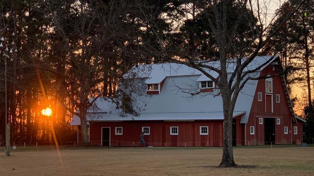 Red barn with white roof at sunset, silhouetted trees in the background.