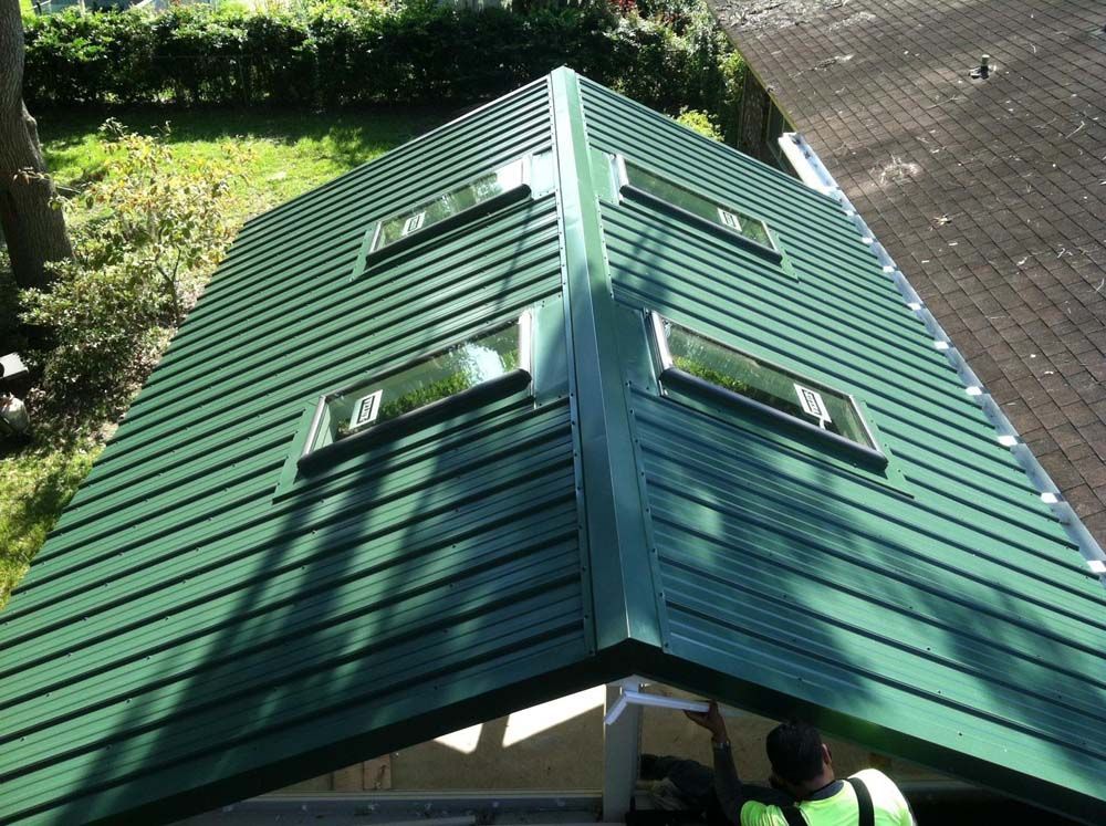 Green metal roof with skylights, viewed from above. Sunlight and shadows highlight the ridges.