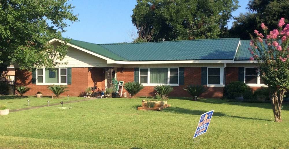 Red brick house with green roof and shutters on a sunny day.