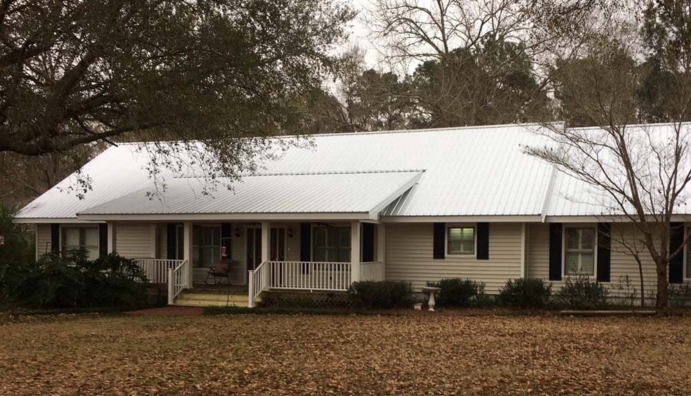 Beige ranch house with a white metal roof and black shutters.