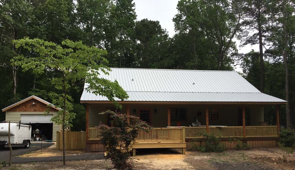 Cabin with wooden deck and a detached garage, set amongst trees.
