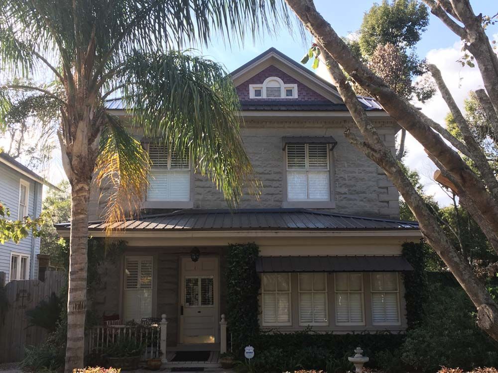 Two-story stone house with dark metal roof, awning over ground floor windows, and a small porch.