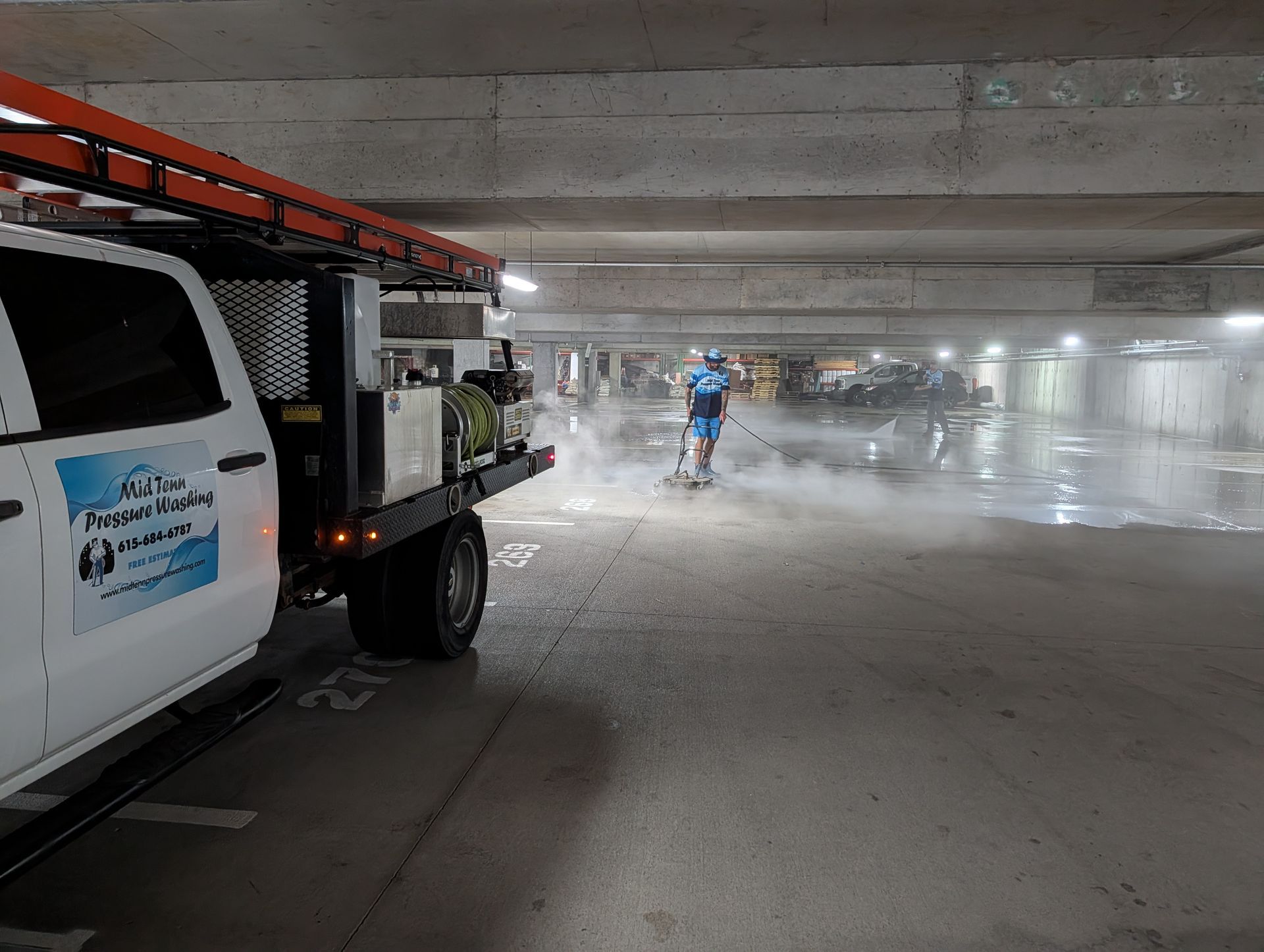 Worker spraying water in a parking garage beside a service truck
