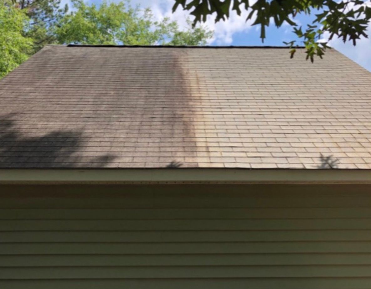 House roof with light shingles, showing a dark patch on the left side and tree leaves overhead