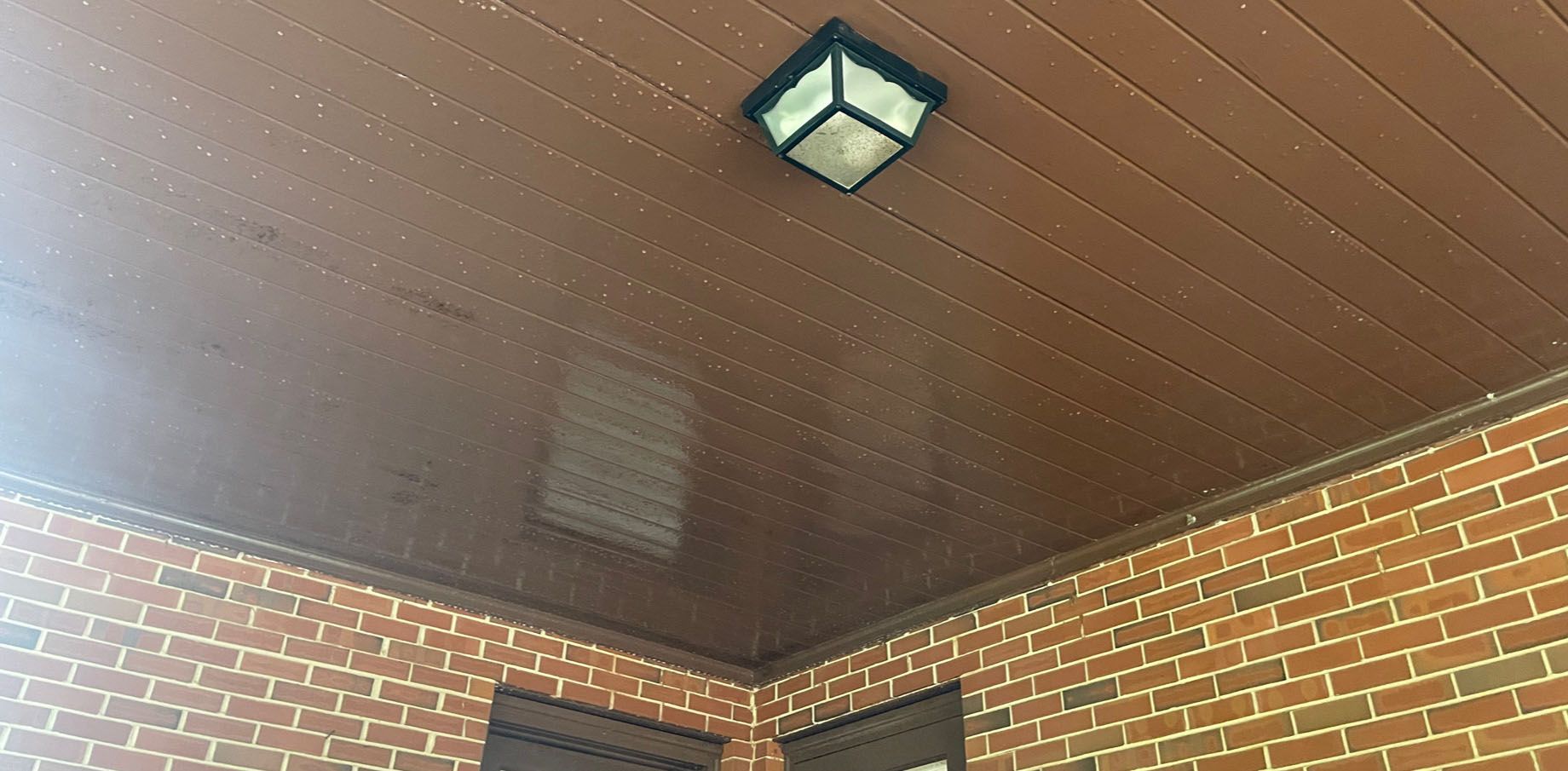 Brown wooden ceiling with a square light fixture and brick wall.