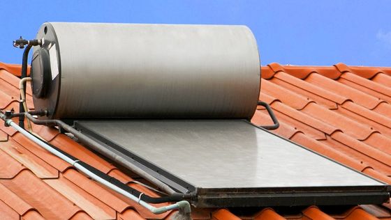 A solar water heater is sitting on top of a tiled roof.