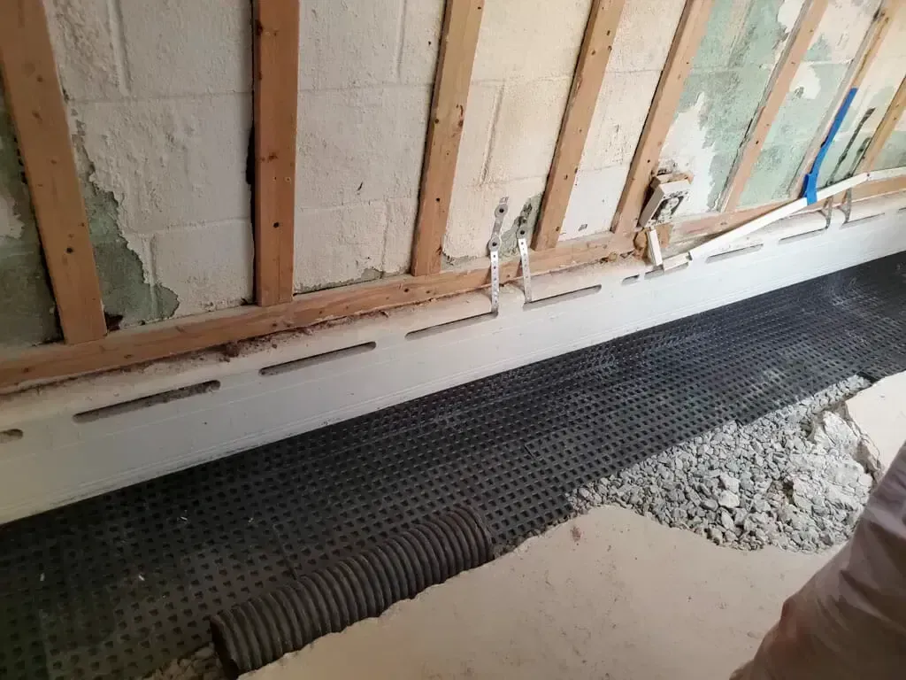 A basement wall during waterproofing, showing a dimpled drainage membrane installed against the wall and floor.
