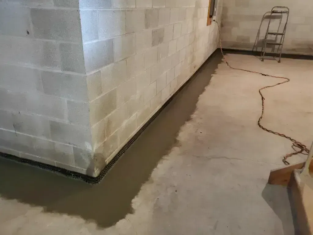 A basement corner shows a floor crack filled with wet concrete sealant along the wall, with a small stepladder nearby.