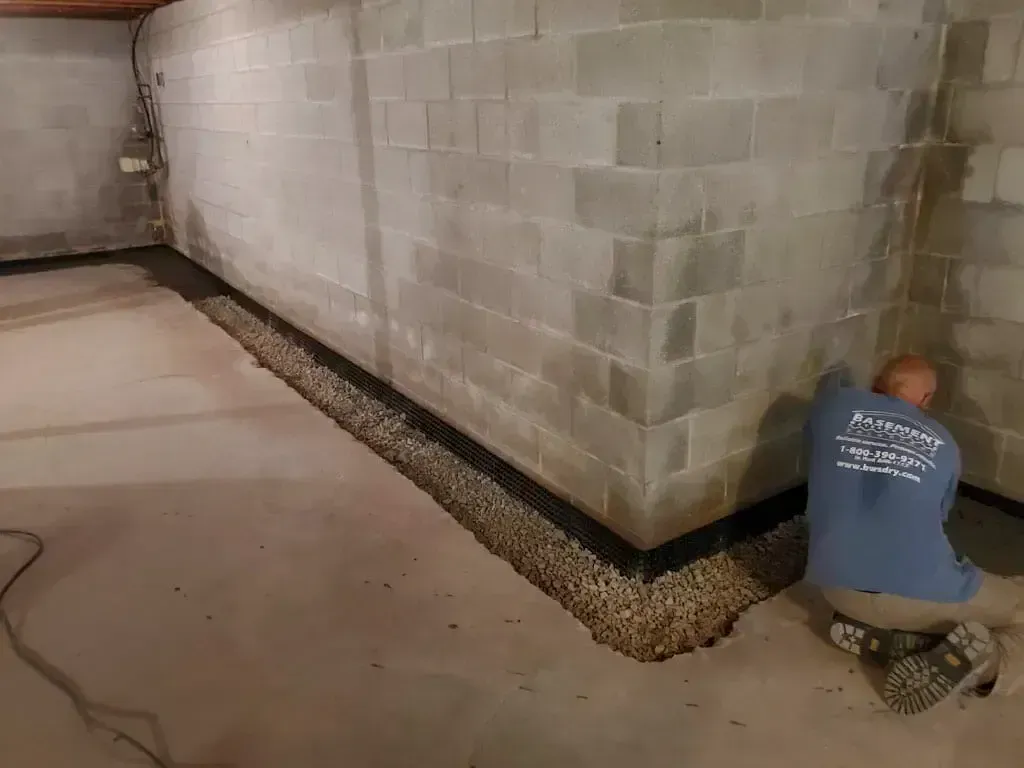 A technician installs a gravel-filled drainage system along the interior wall of a concrete block basement.