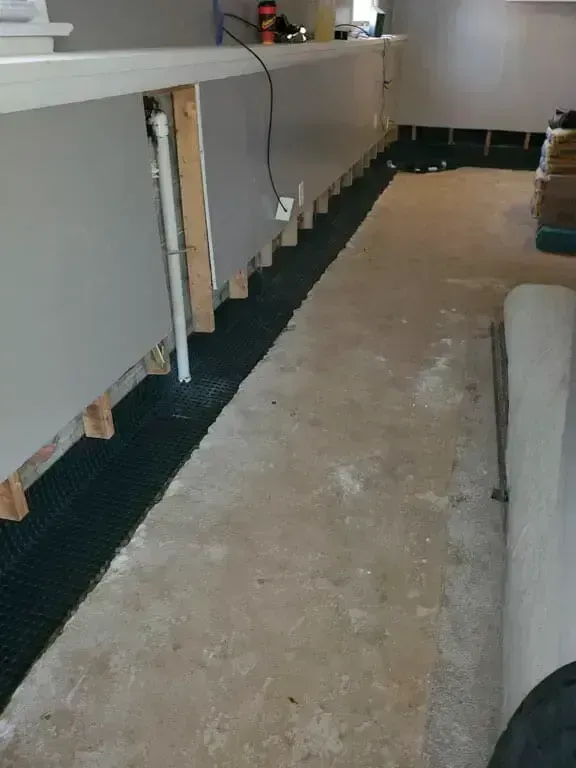 A view of an unfinished room with a long counter supported by wooden studs above a dark, unfinished flooring strip.