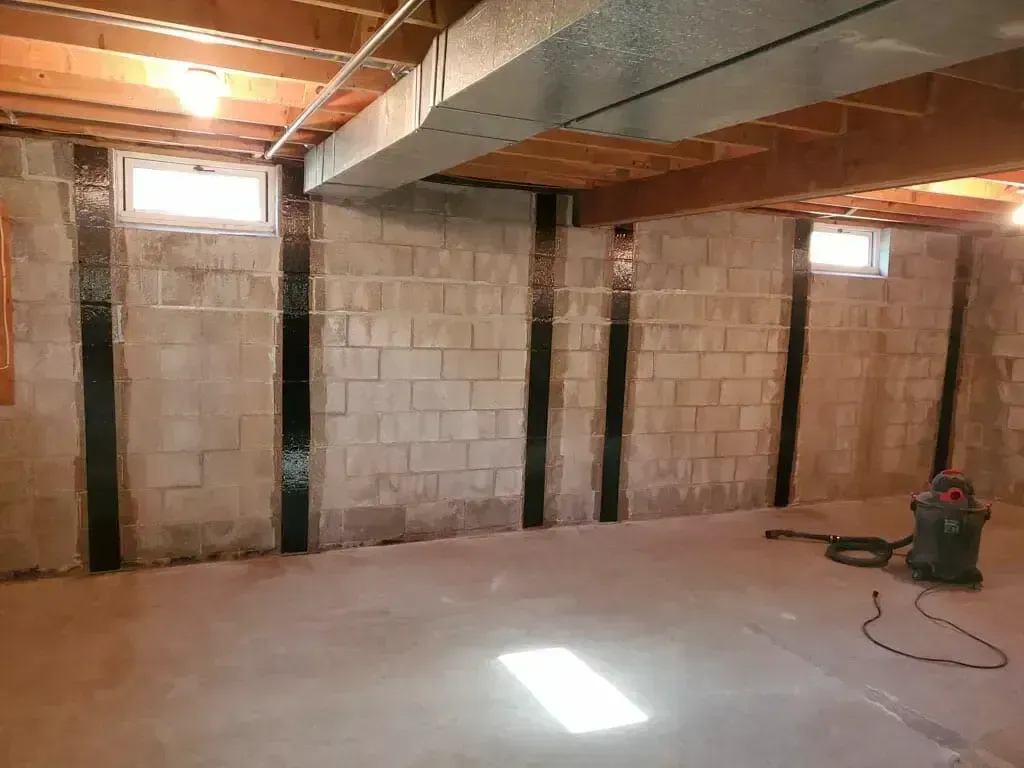 A basement wall made of concrete blocks, reinforced with vertical carbon fiber strips, with a shop vacuum on the floor.