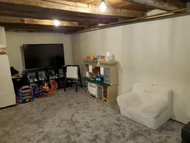 A finished basement playroom with grey carpet, a television, a toy kitchen, and a white fuzzy armchair.