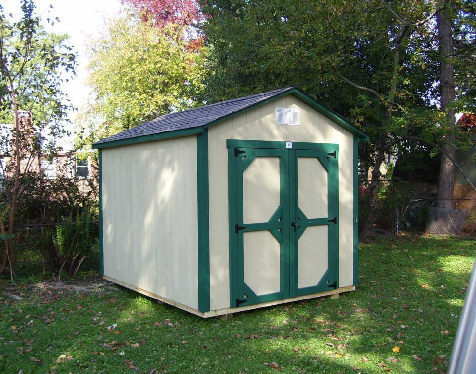 A white shed with green trim is sitting in the grass