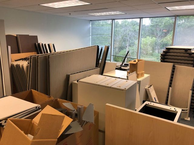 Office storage room with stacked cardboard boxes, panels, and desks by large windows