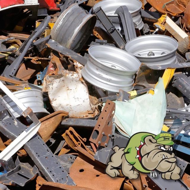 Piles of scrap metal and car rims in a junkyard, with a green cartoon monster sticker in the corner.