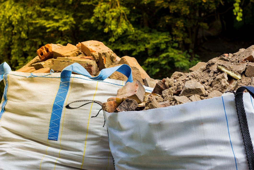 White construction bags filled with rubble and rocks in a wooded outdoor area