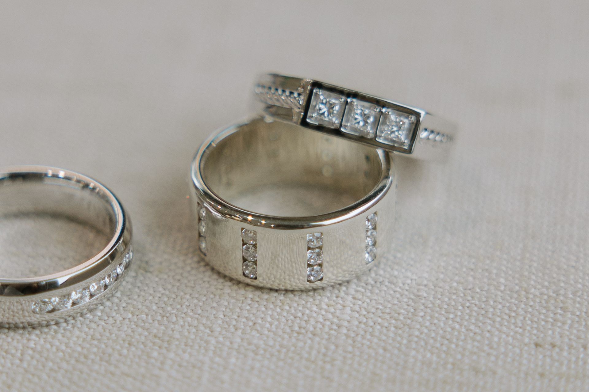 Three silver rings with diamonds on a beige surface.