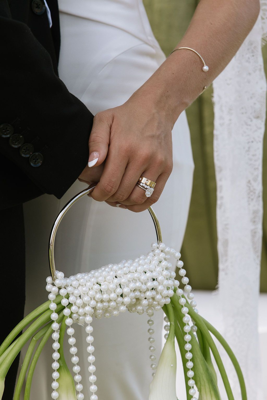 Bride holding groom's arm, wearing a ring, carrying a ring-handled bouquet of pearls and lilies.
